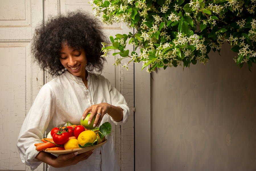 Ospite sorridente con un cesto di frutta e verdura di stagione accanto ai gelsomini